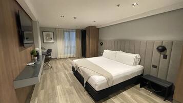 A modern hotel room with a large bed, a desk, a chair, and a TV.