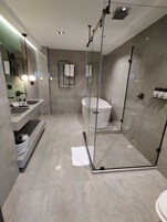 Ein modernes Badezimmer mit einer Glaskabine zur Dusche, einer freistehenden Badewanne und einem Waschtisch mit Spüle und Spiegel.