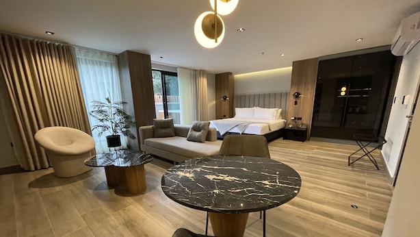 A modern hotel room with a sofa, a round table, a chair, a bed, and a large window. - HOTEL SELIS (Medellín)