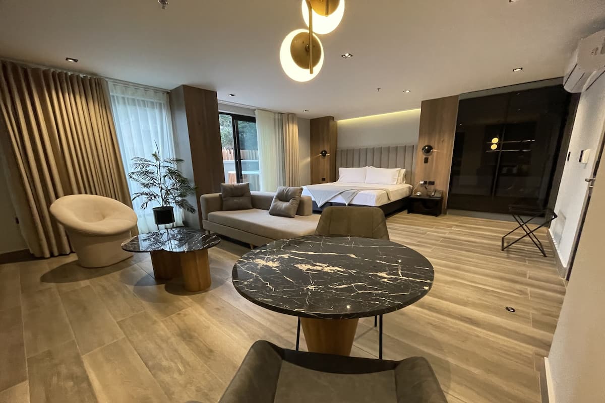 A modern hotel room with a sofa, a round table, a chair, a bed, and a large window.