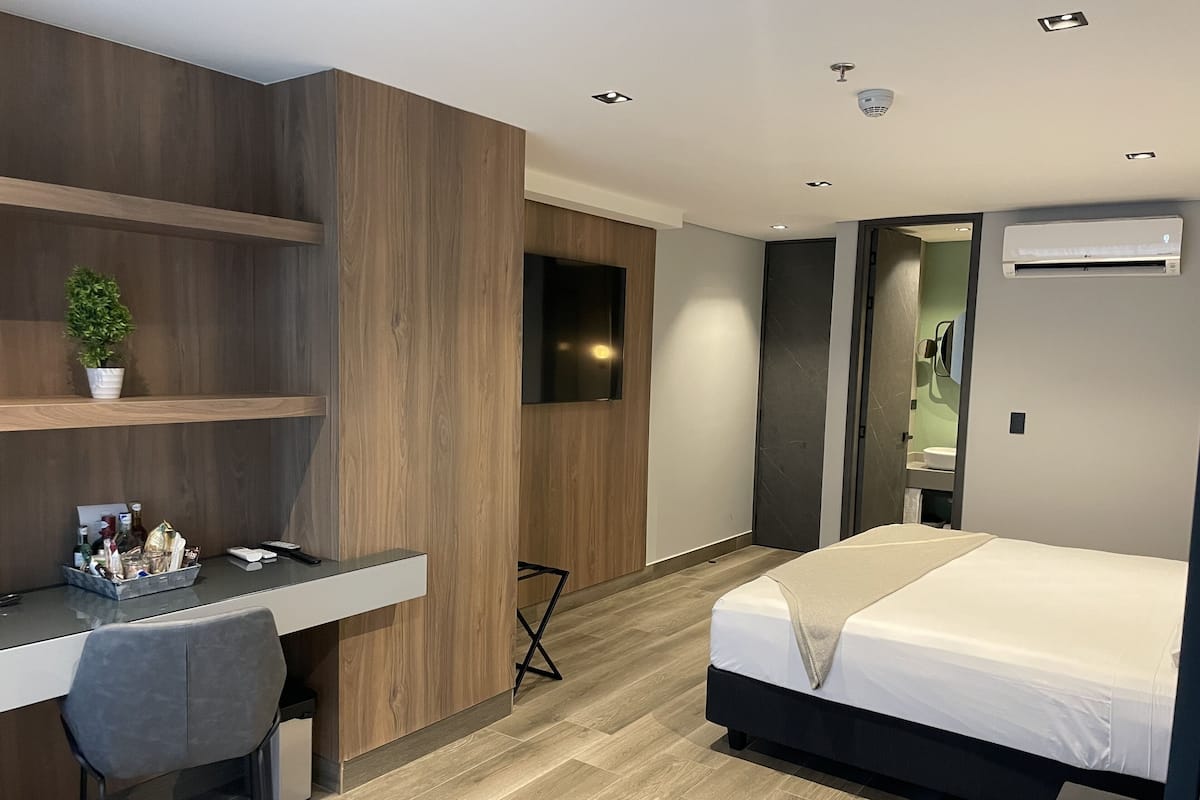 A modern hotel room with a wooden desk, a bed, and a TV mounted on the wall.