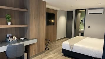 Quarto de hotel moderno com escrivaninha de madeira, uma cama e televisão na parede.