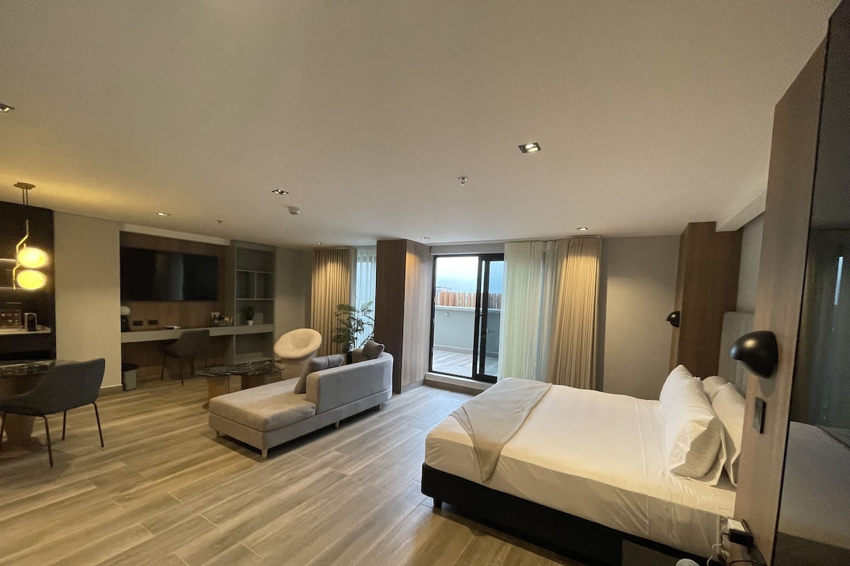 A modern hotel room with a large bed, a sofa, a desk, and a balcony.