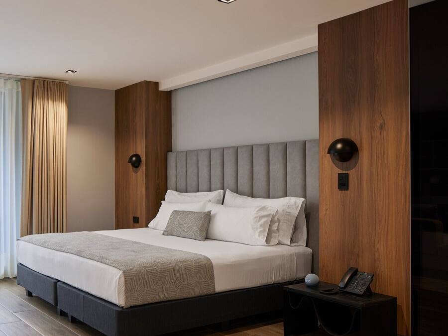 Un dormitorio moderno con una cama grande, paneles de madera y una mesita de noche con un teléfono.