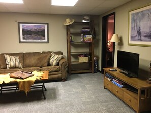 A living room with a brown leather couch, a coffee table, a TV on a wooden stand, a bookshelf, and a framed picture of a landscape.