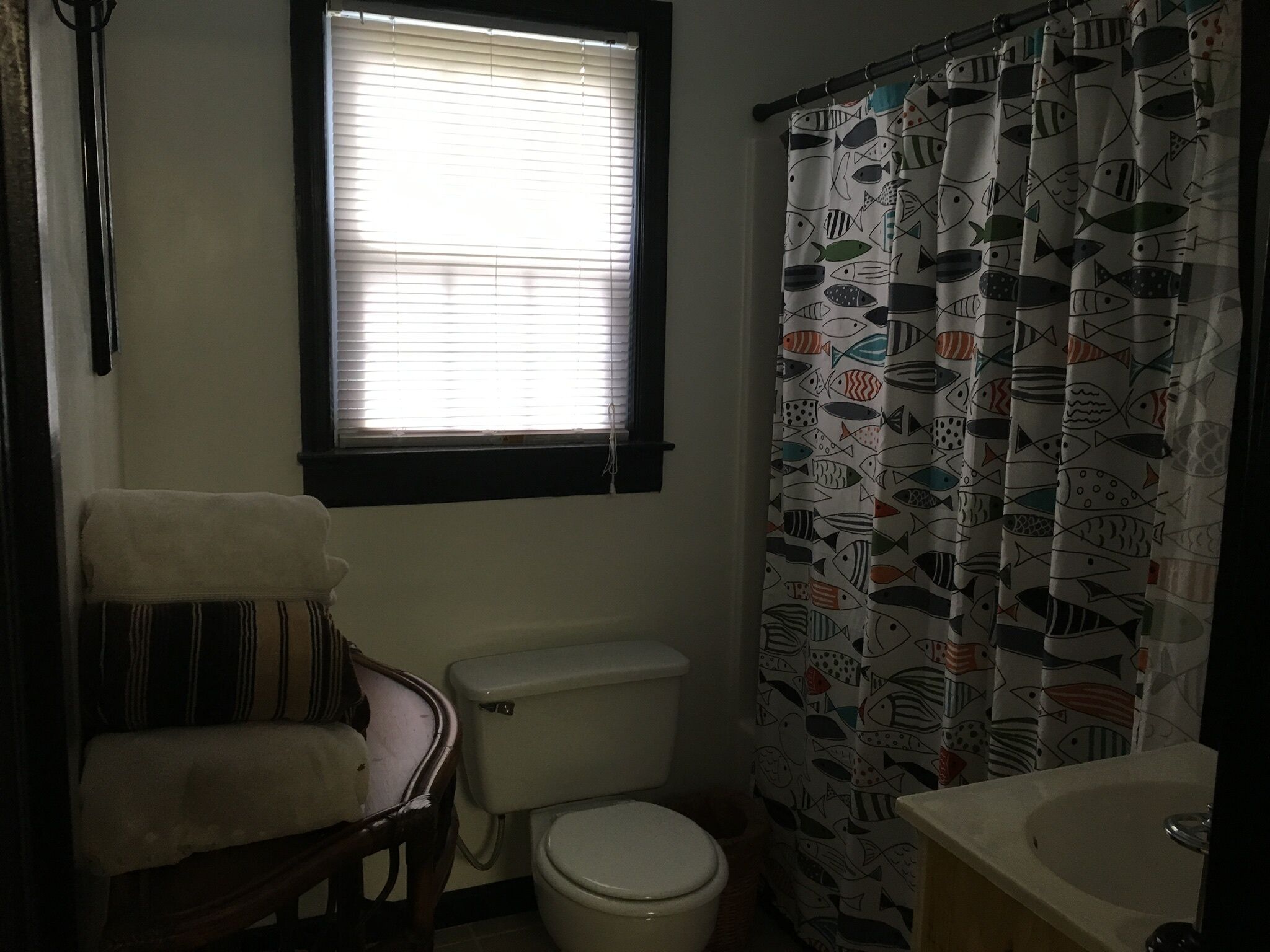 A bathroom with a toilet, a window, and a shower curtain with a fish pattern.