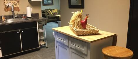 A kitchen with a wooden counter, a sink, and a bar stool. There is a woven basket with a rooster decoration on the counter.