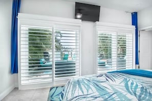 A bedroom with a bed, white shutters, and a view of greenery outside.
