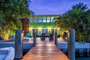 A wooden deck leading to a building with a green facade and large windows. There are outdoor seating areas with chairs and tables.