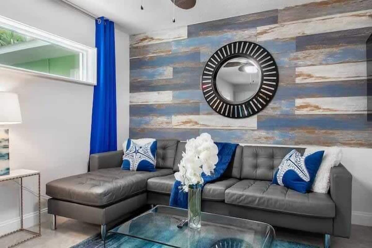 A modern living room with a sectional sofa, a glass coffee table, and a decorative mirror on a textured wall.