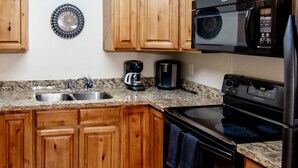 Una cucina con mobili in legno, un piano di lavoro in granito, un fornello nero, un forno a microonde e una macchina da caffè.