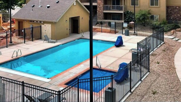 Un edificio a più piani con piscina, circondato da una recinzione, con le montagne sullo sfondo.