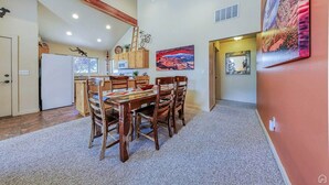 A dining area with a wooden table and chairs, a kitchen with wooden cabinets, and a painting on the wall.