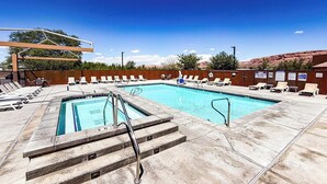 A swimming pool with lounge chairs, a wooden deck, and a clear blue sky.