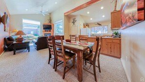 A spacious living room with a fireplace, a dining area with wooden furniture, and a kitchen with wooden cabinets and a large window.