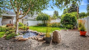 A backyard with a small pond, gravel paths, and various plants and trees. - Centrally located, family and furry friendly fun! (Yakima)