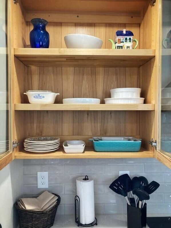 Un meuble de cuisine en bois, doté d’étagères où sont rangés différents plats, et un vase bleu.