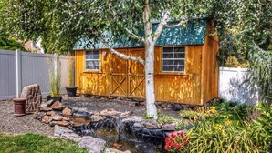 A wooden shed with a green roof, a small waterfall feature, and surrounding garden plants. - Centrally located, family and furry friendly fun! (Yakima)