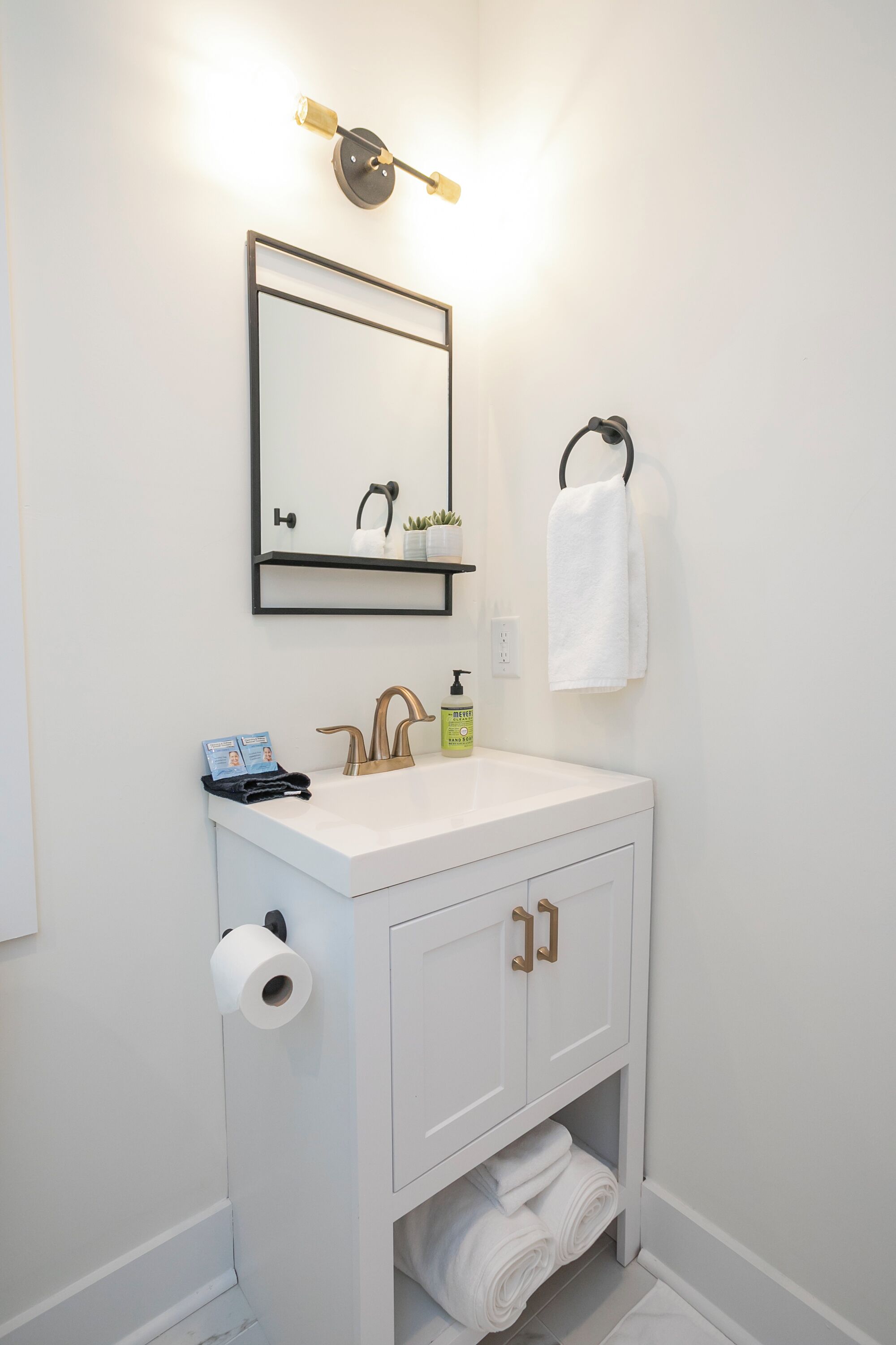 Ein Badezimmer mit weißem Waschbecken, einem Spiegel, einem Handtuchhalter und einem Toilettenpapierhalter.