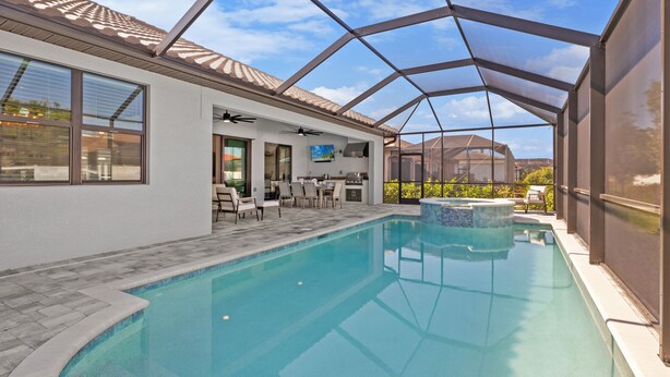 A covered outdoor swimming pool with a patio area, a kitchen, and a large window overlooking the pool.