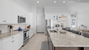 A modern kitchen with white cabinetry, stainless steel appliances, and a large island with a sink.