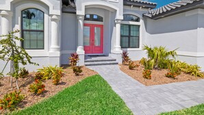 A modern house with a red door, white columns, and a well-maintained garden.