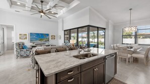 A modern kitchen with a large island, dark cabinetry, and a dining area with a glass-enclosed patio.