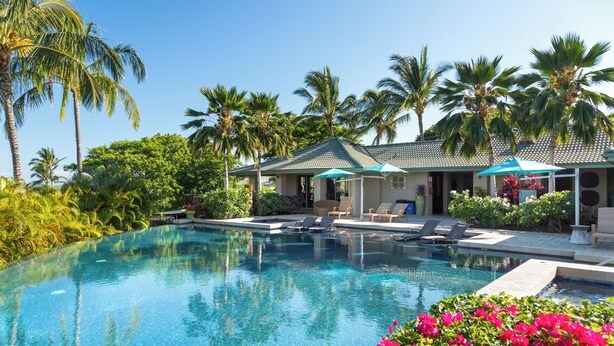 A swimming pool with lounge chairs and umbrellas, surrounded by palm trees and lush greenery. - Mauna Kea Waiulaula I201- Stunning Ocean & Golf Views - New Furnishings (Kamuela)