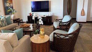 A modern living room with a sofa, chairs, a coffee table, a TV, and decorative items. - Mauna Kea Waiulaula I201- Stunning Ocean & Golf Views - New Furnishings (Kamuela)