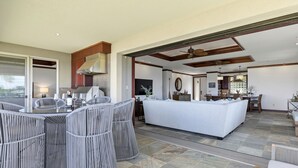 A spacious living area with a large white sofa, wicker chairs, and a kitchen in the background. - Mauna Kea Waiulaula I201- Stunning Ocean & Golf Views - New Furnishings (Kamuela)