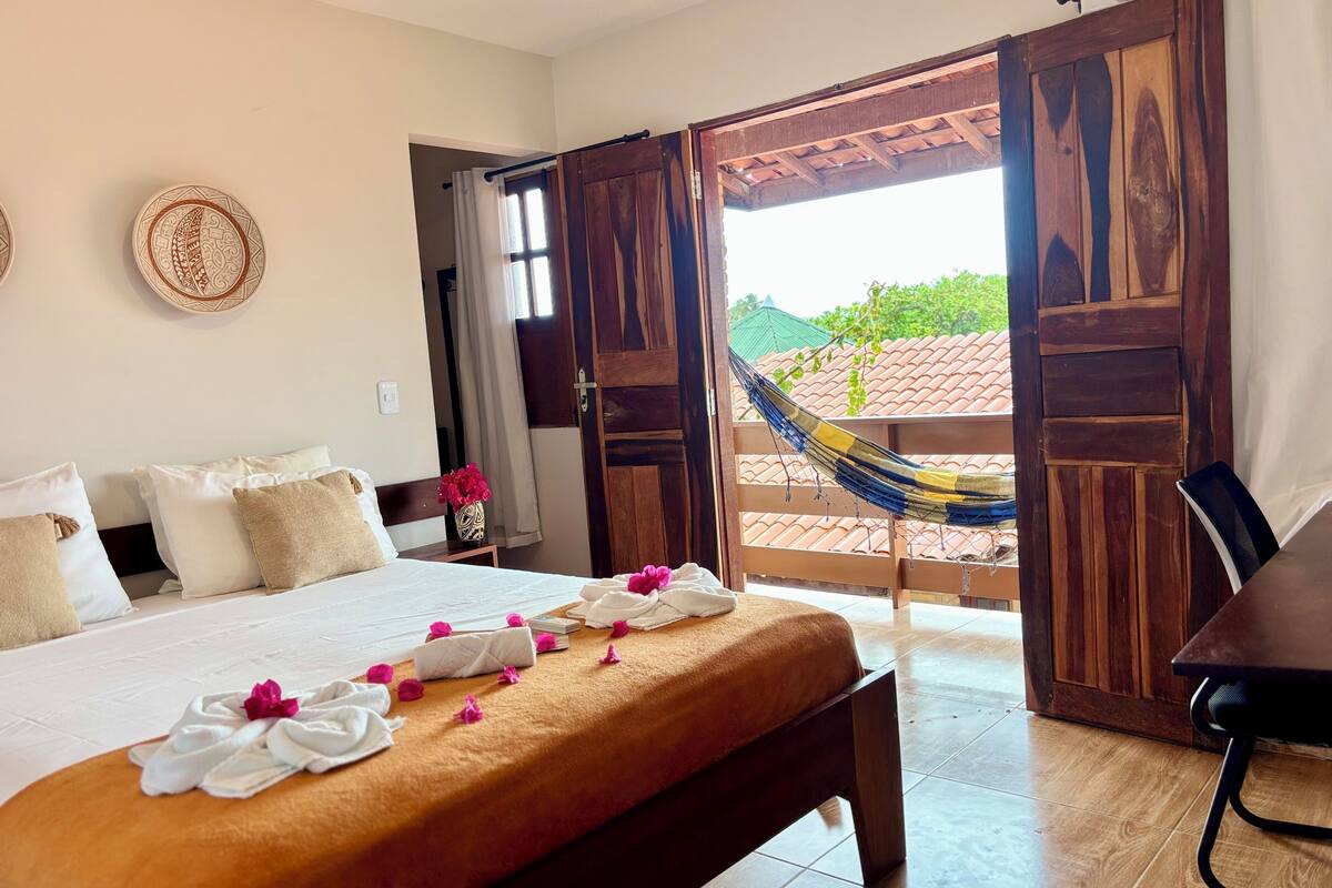 Una habitación de hotel con cama, almohadas, un banco, una mesa y una hamaca.