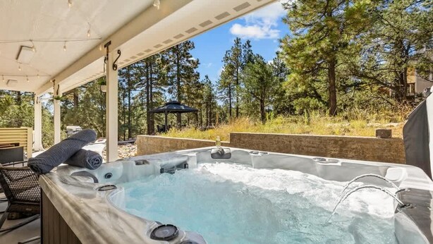 A hot tub under a covered patio with a view of a forested area. - Craftsman | Int Designed | AC | Hottub | Epic yard (Flagstaff)