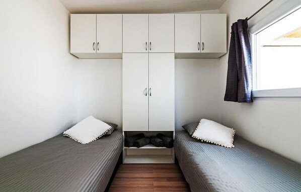 Ein kleines Zimmer mit zwei Einzelbetten, einem Kleiderschrank und einem Fenster mit Vorhängen.