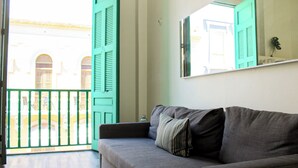 Ein Zimmer mit einer grauen Couch, einer grünen Tür und einem Balkon mit Blick auf Gebäude.