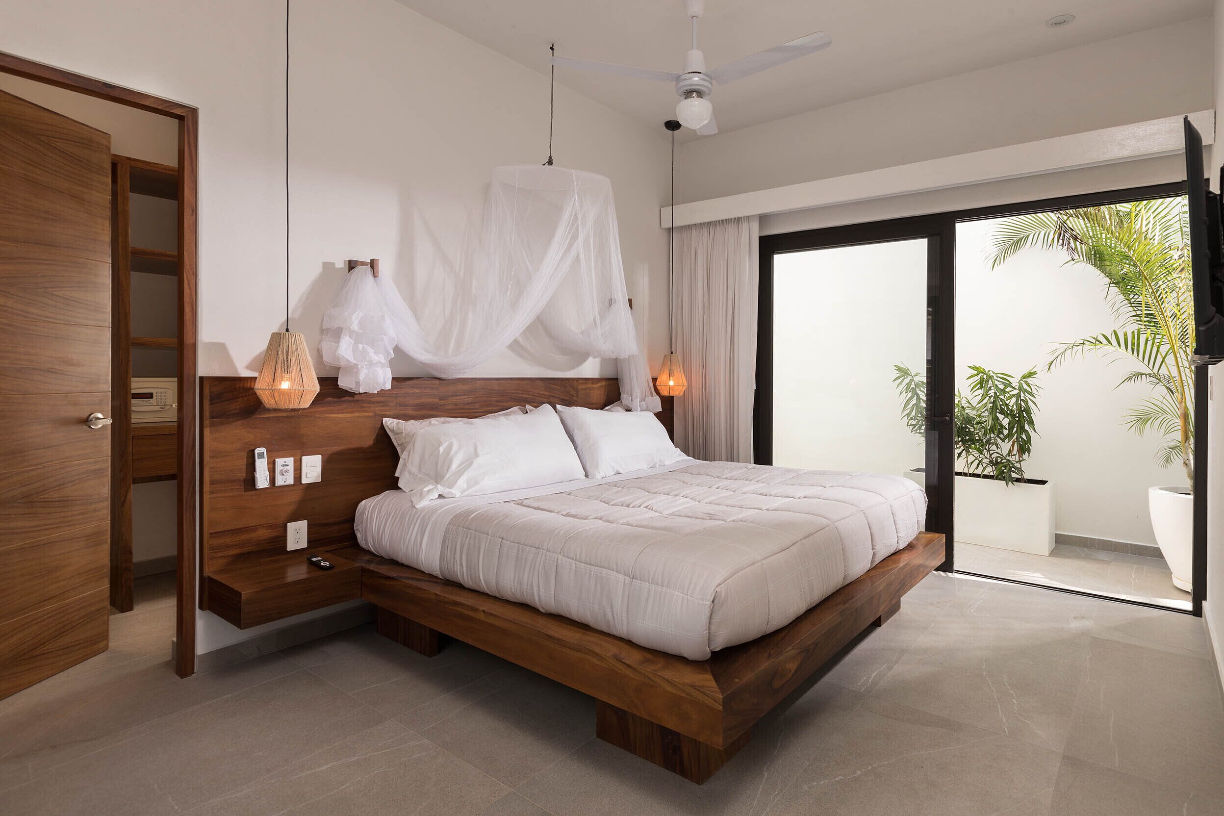 Un dormitorio moderno con una cama de madera, lámparas de noche, un ventilador de techo y vistas al exterior.