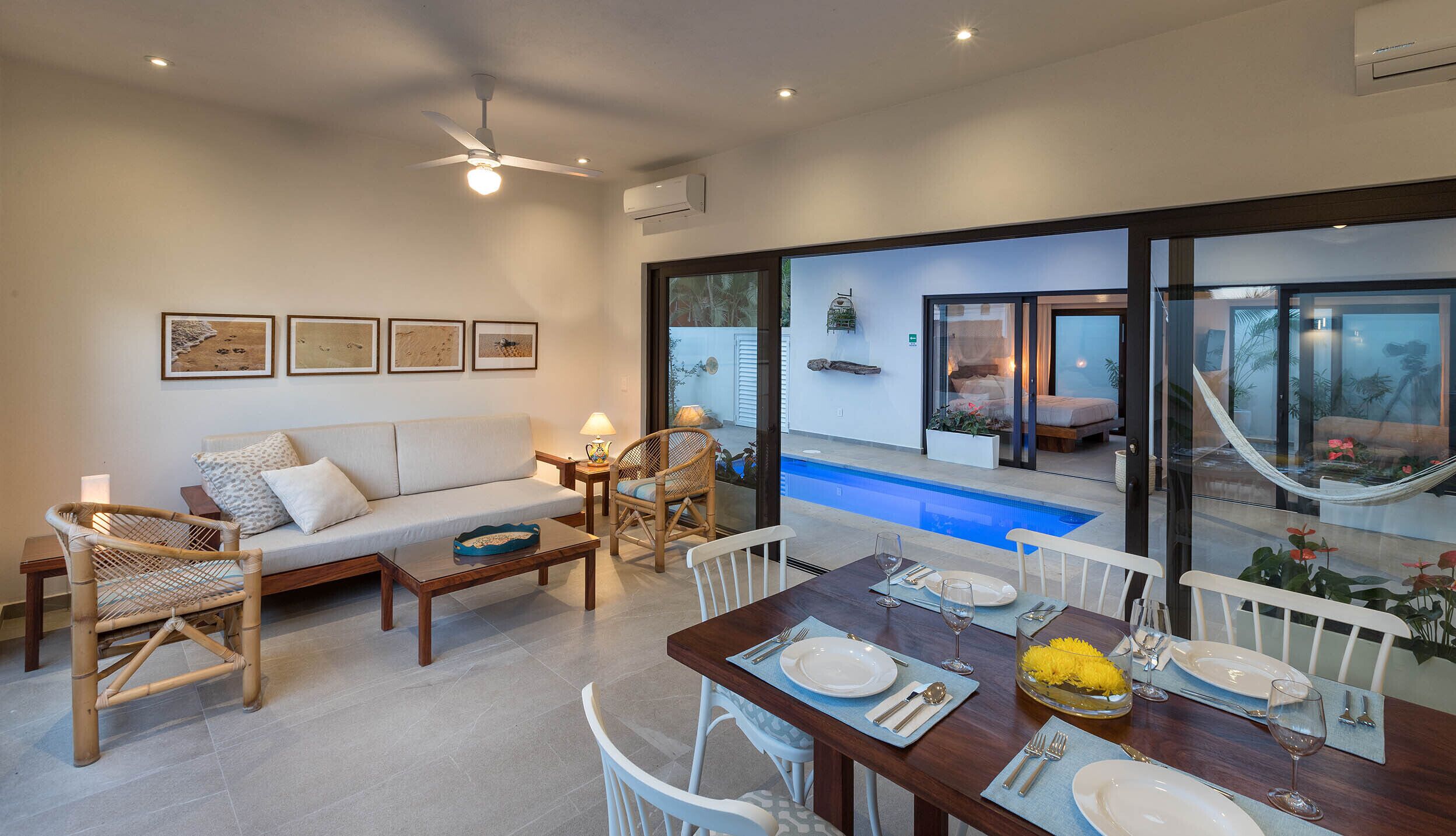 Una sala de estar moderna con un sofá, una mesa de comedor para dos personas y vista a una piscina y zona de estar exterior.