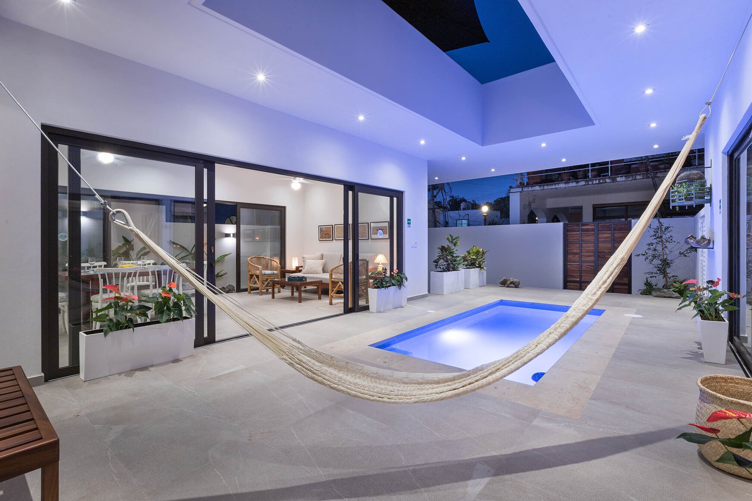Un espacio exterior moderno con piscina, zona de estar y una hamaca.