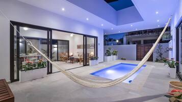 Un espacio exterior moderno con piscina, zona de estar y una hamaca.