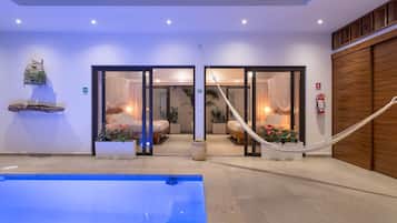 Un área de piscina interior moderna con vistas despejadas, una hamaca y un rincón de descanso con cojines y plantas.