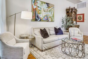 Una sala de estar con sofá, sillones, una mesa de centro, una lámpara de pie, un cuadro y un aparador decorativo.