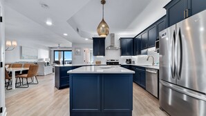 Een moderne keuken met donkerblauwe kastjes, een roestvrijstalen koelkast en een centraal keukenblok.