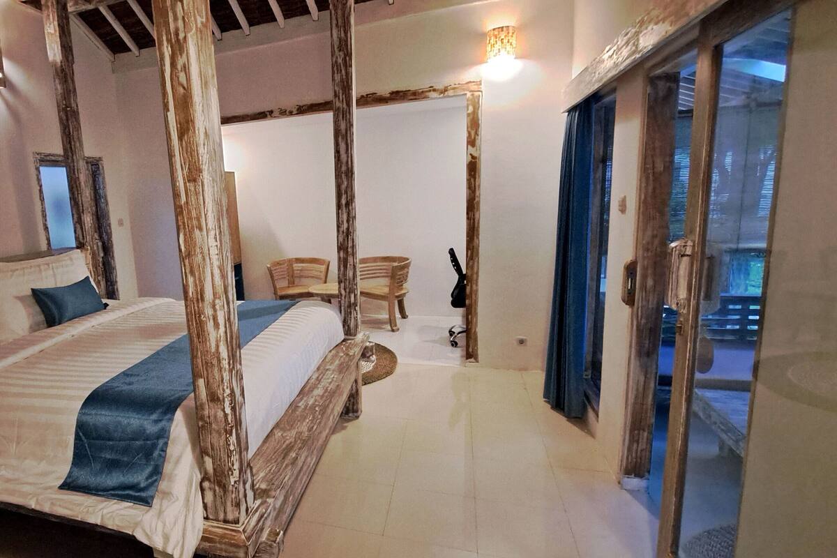 Une chambre à coucher avec un grand lit, des meubles en bois, un tableau et une vue à travers une porte vitrée.