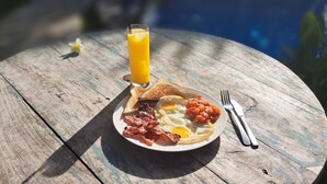 A breakfast plate with toast, eggs, bacon, and tomatoes, accompanied by a glass of orange juice on a wooden table.