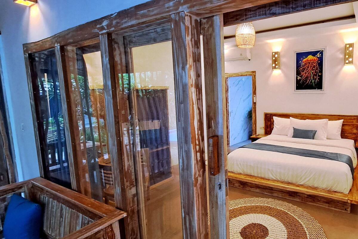 Une chambre avec un lit en bois, une grande fenêtre et un luminaire fixé au mur.