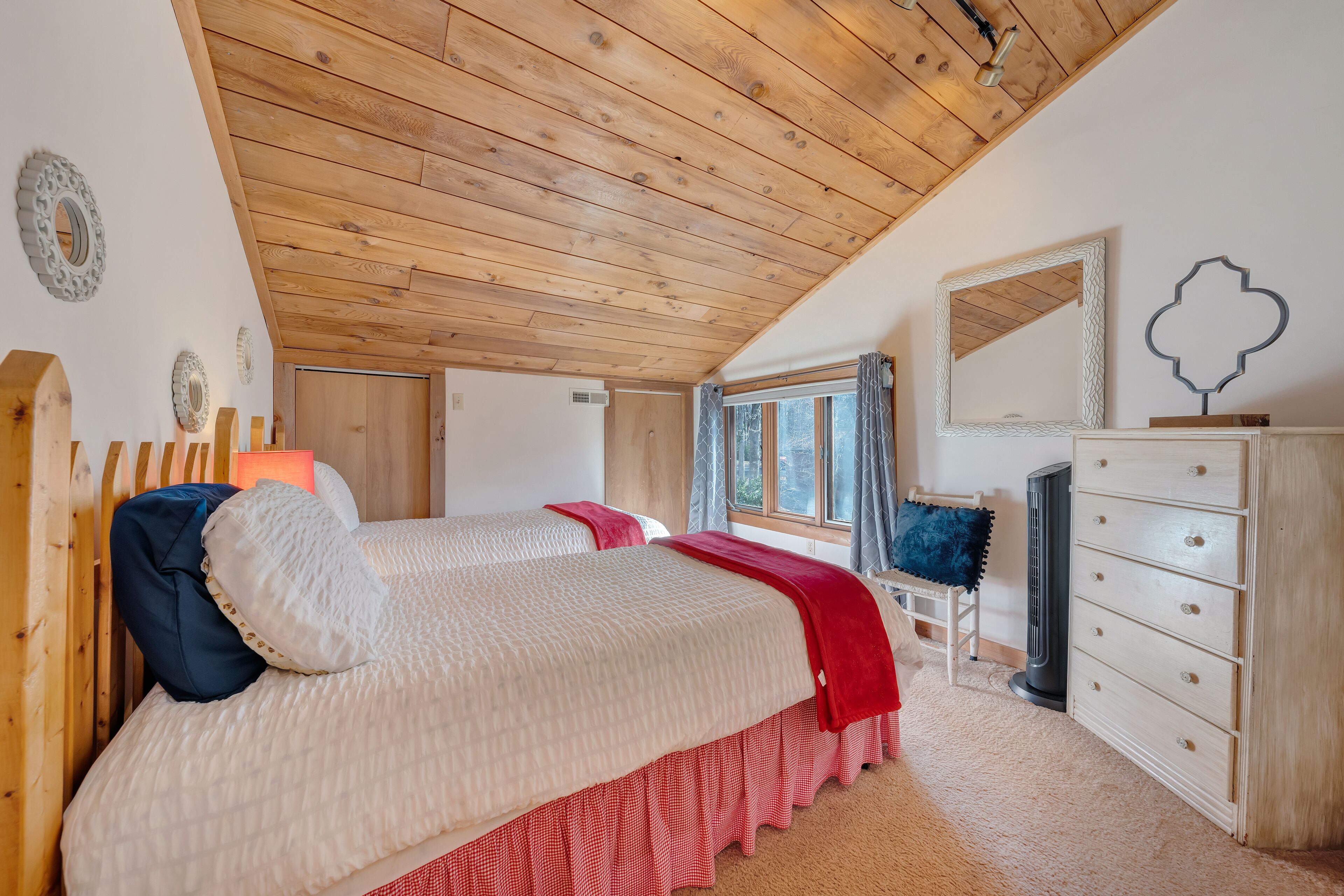 A bedroom with a wooden ceiling, a bed with a red and white bedspread, a dresser, and a mirror.