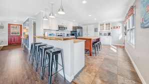 Una cocina moderna con armarios blancos, electrodomésticos de acero inoxidable y una isla central con taburetes de bar.