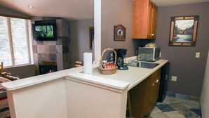 Cocina compacta con protector contra salpicaduras de piedra, televisor de pantalla plana, chimenea y comedor con ventana.