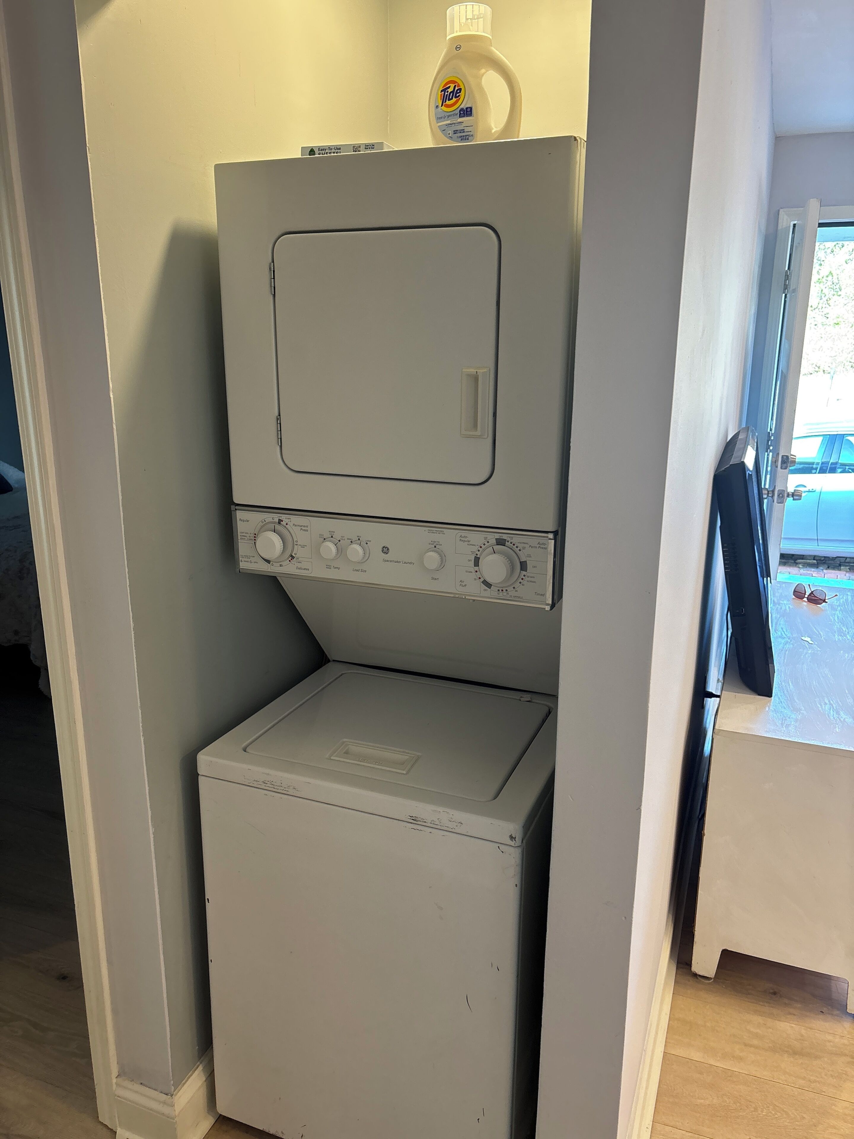 Eine kompakte, weiße Waschmaschine mit Bedienfeld, platziert in einer schmalen Nische, mit einer Flasche Tide Waschmittel darauf.