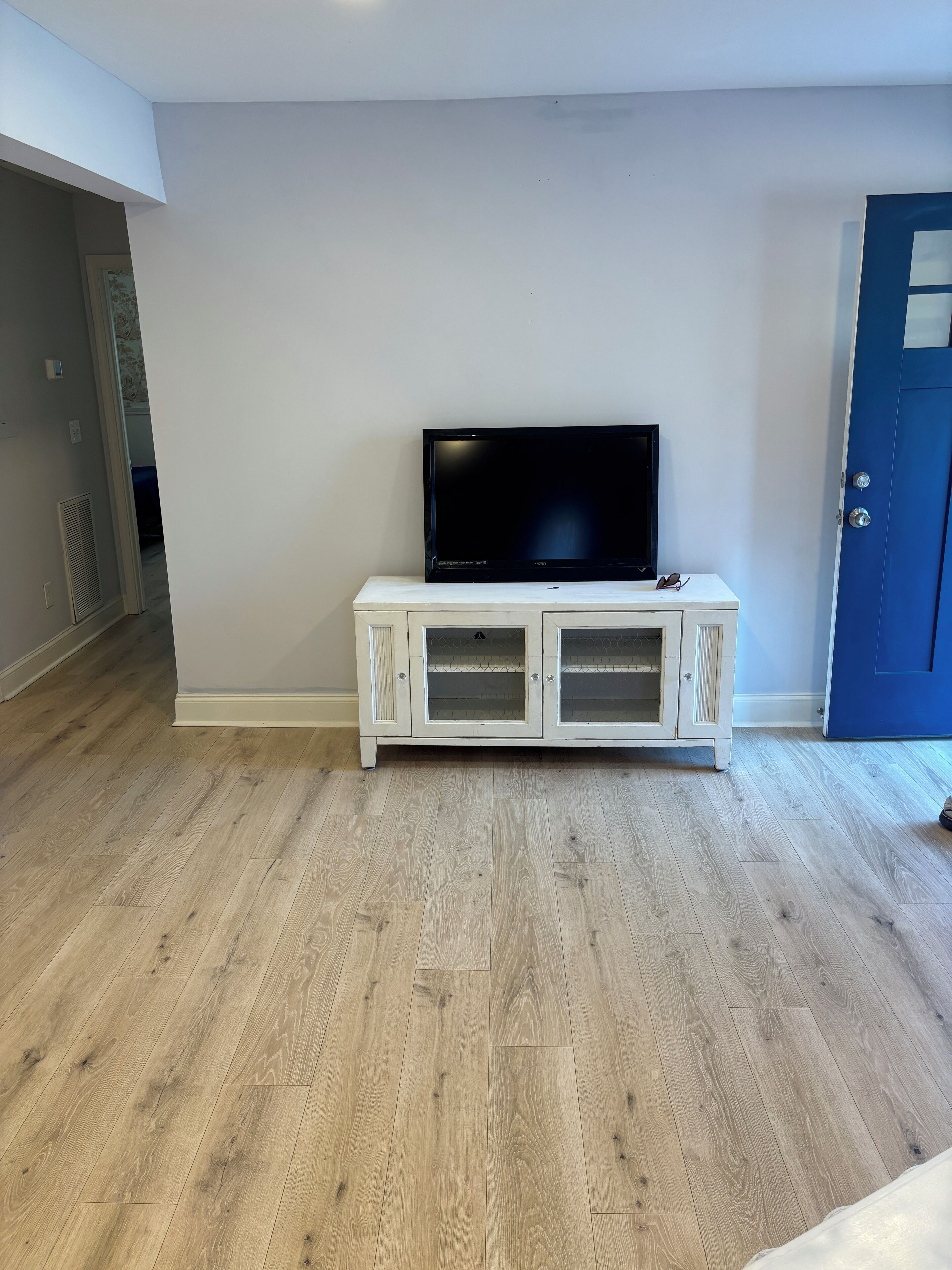 A room with a flat-screen TV on a white cabinet, wooden flooring, and a blue door.