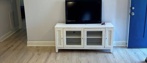 A room with a flat-screen TV on a white cabinet, wooden flooring, and a blue door.
